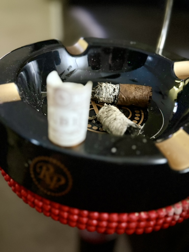 Rocky Patel LB1 Robusto resting as a short nub with its band removed in a black Rocky Patel ashtray.
