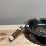 Rocky Patel Dark Star Robusto resting against a black RP ashtray on a wooden shelf.