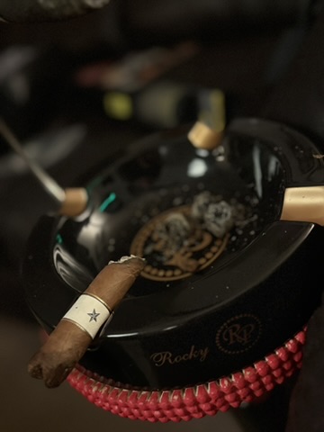Short Rocky Patel Dark Star Robusto segment with white band resting on a black Rocky Patel ashtray.