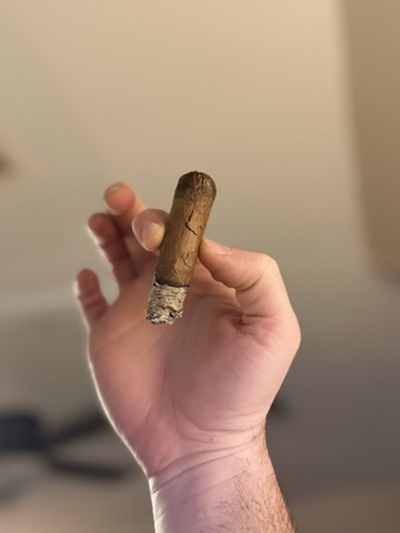 Rocky Patel Dark Star Robusto held aloft with a column of ash and a vertical wrapper crack.