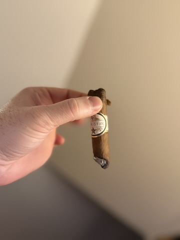 Hand holding a smoked Rocky Patel Dark Star Robusto with a widening crack near the cap.