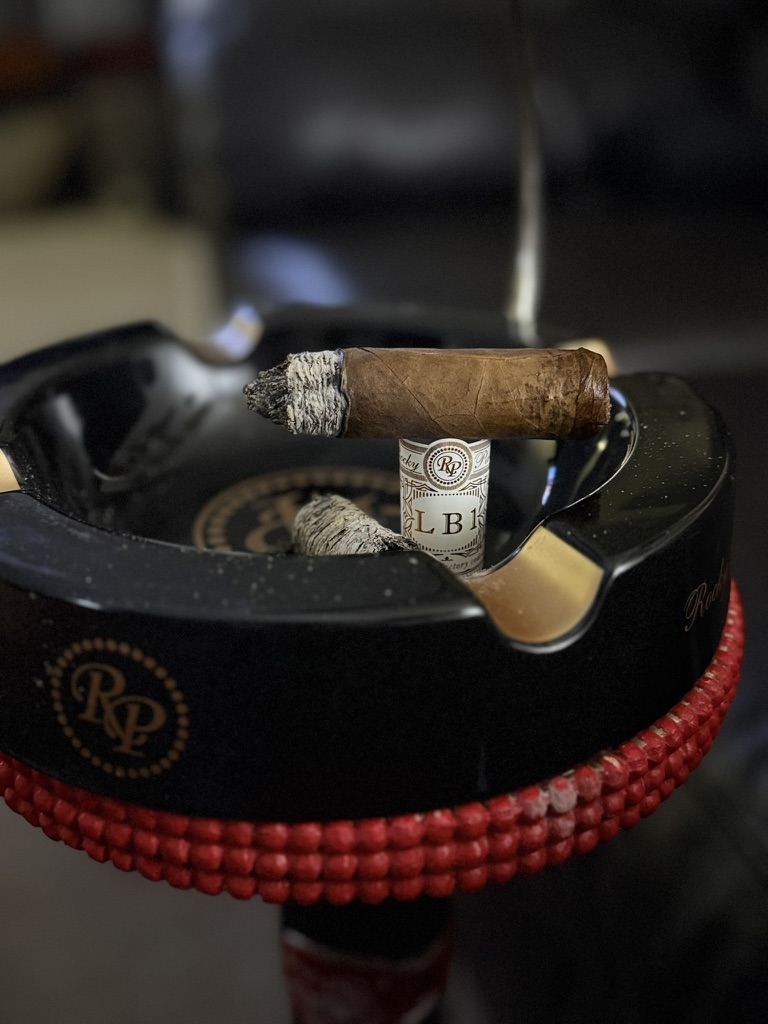 Rocky Patel LB1 Robusto balanced on its band above the Rocky Patel ashtray logo with a long ash.