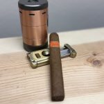 Cain Daytona Box Pressed Toro on wooden surface with copper torch lighter and metal cigar cutter
