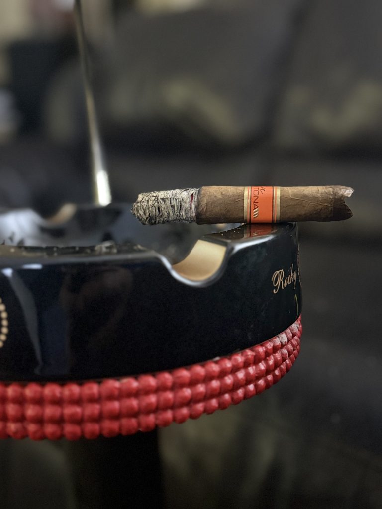 Cain Daytona Box Pressed Toro on a black Rocky Patel ashtray with orange band visible and long ash above the tray