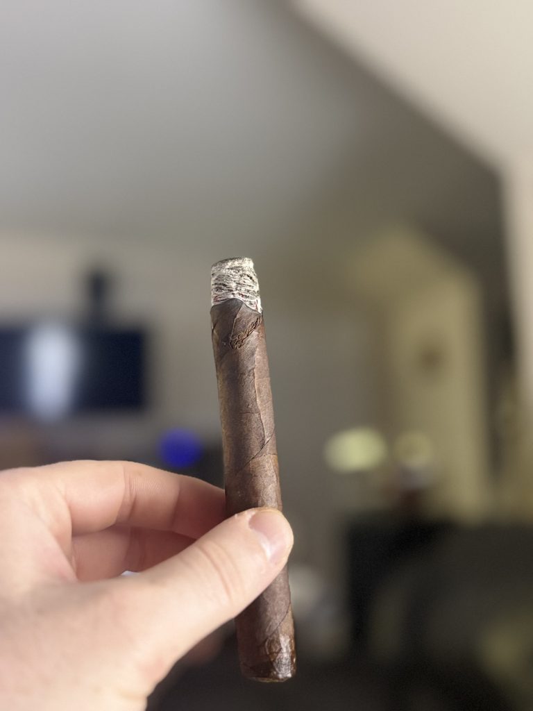 Hand holding an Alec Bradley Black Market Toro with ash forming on the tip in an indoor lounge