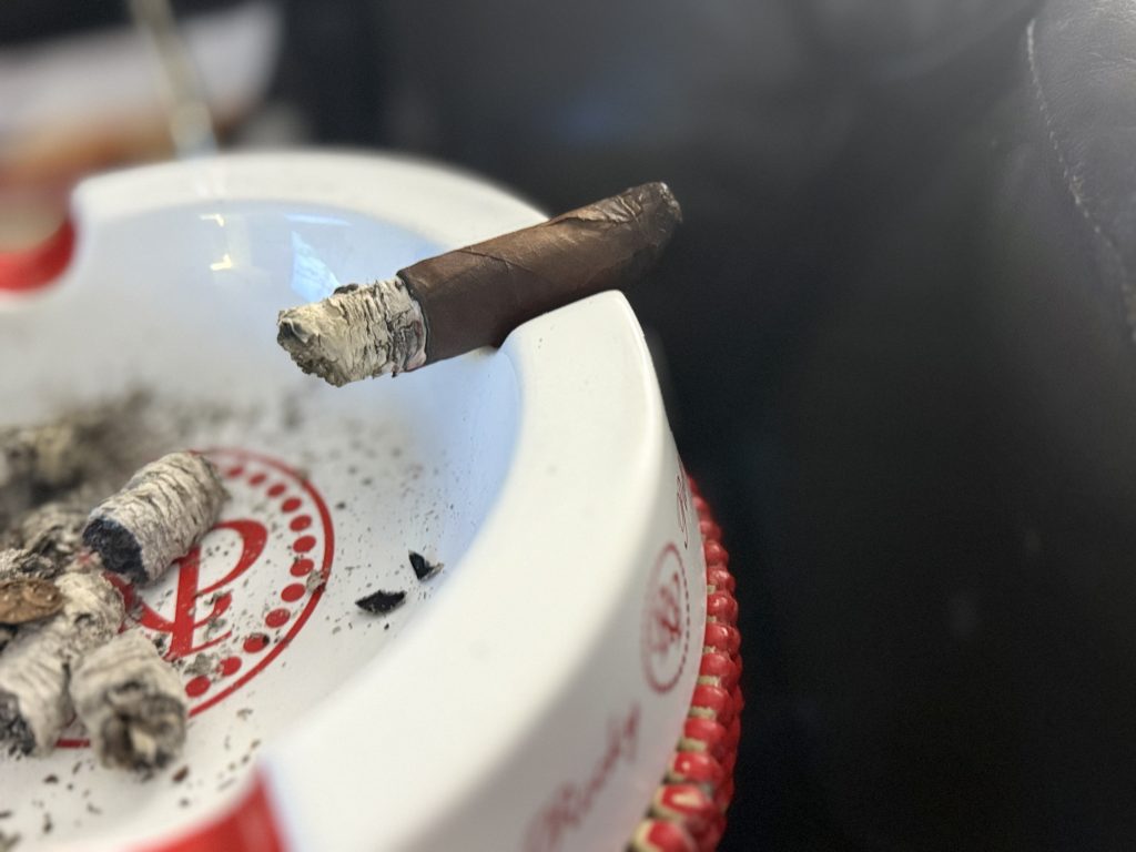 Alec Bradley Black Market Toro resting on an ashtray with long ash and fallen ash nearby