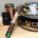 My Father La Opulencia Toro cigar with green foot ribbon resting on a wooden surface beside an Arturo Fuente ashtray and cigar accessories.