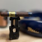 Macanudo Emissary France cigar resting horizontally on a black cigar cutter stand with a blue ashtray in the background.
