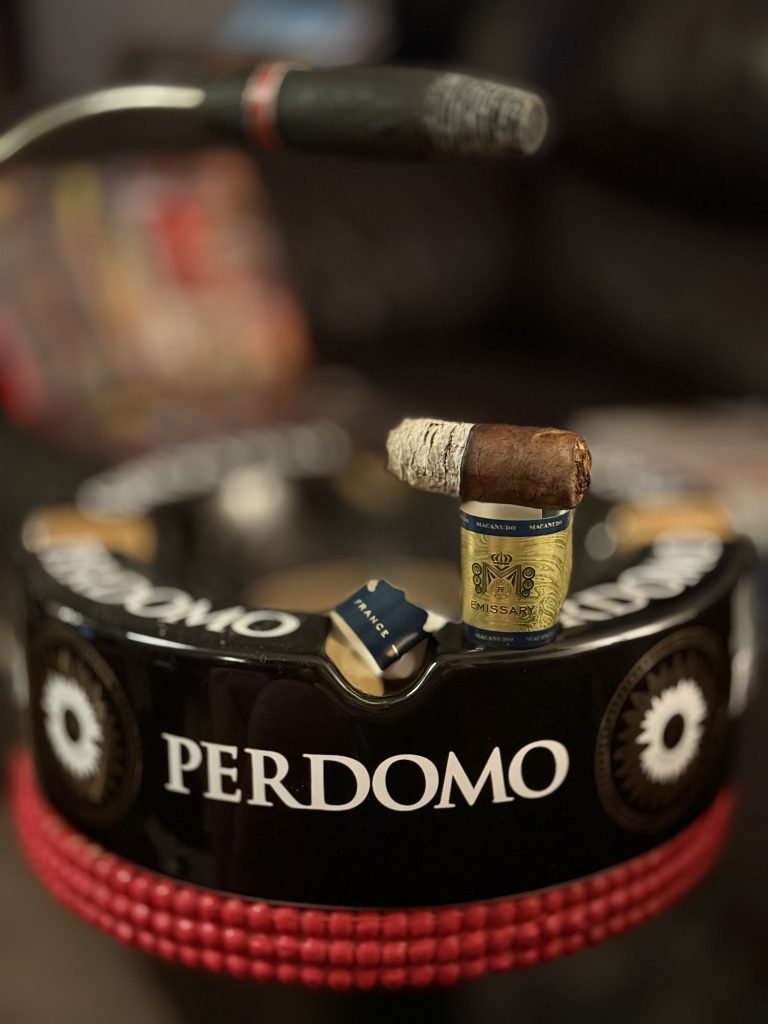 Partially smoked Macanudo Emissary France resting on a Perdomo ashtray with bands in front.