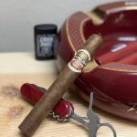 La Palina 125 Años Toro resting on a red ceramic cigar ashtray beside a red Victorinox cigar knife before being lit.