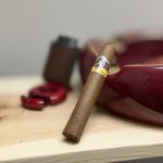 Unlit Aladino Corojo Robusto resting against a red cigar ashtray before The Evening Draw review.