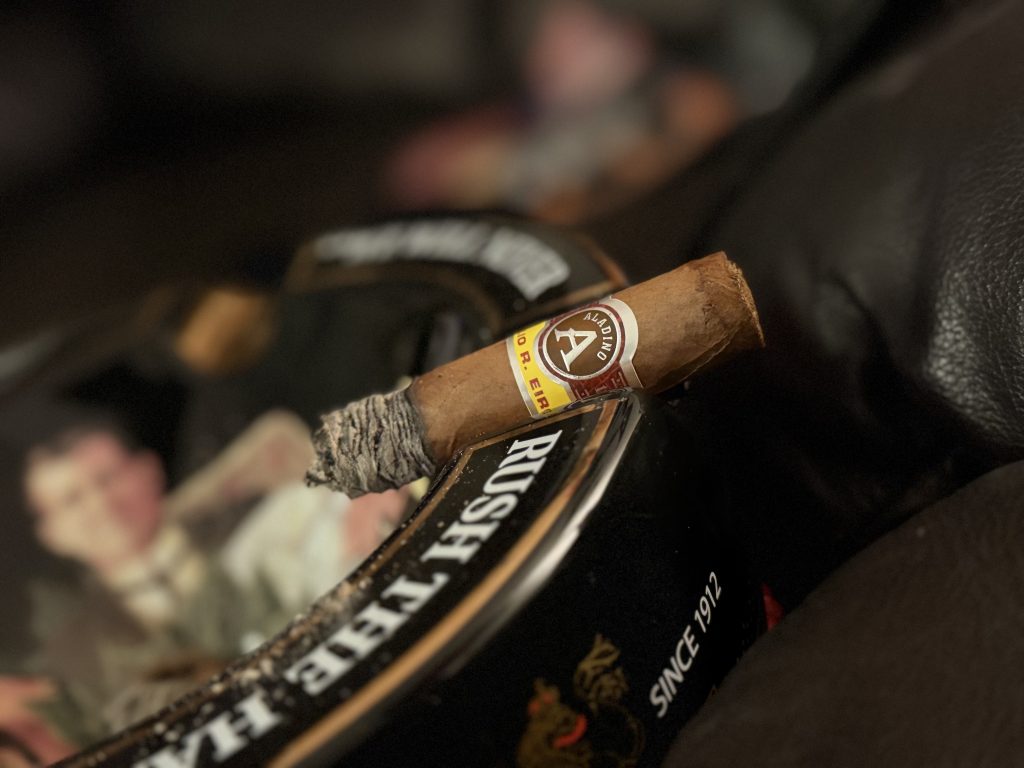 Lit Aladino Corojo Robusto with developed ash resting on a cigar ashtray during the review.