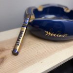 Unlit Rocky Patel Sapphire cigar resting on a light wood surface beside a dark blue Weller ashtray.