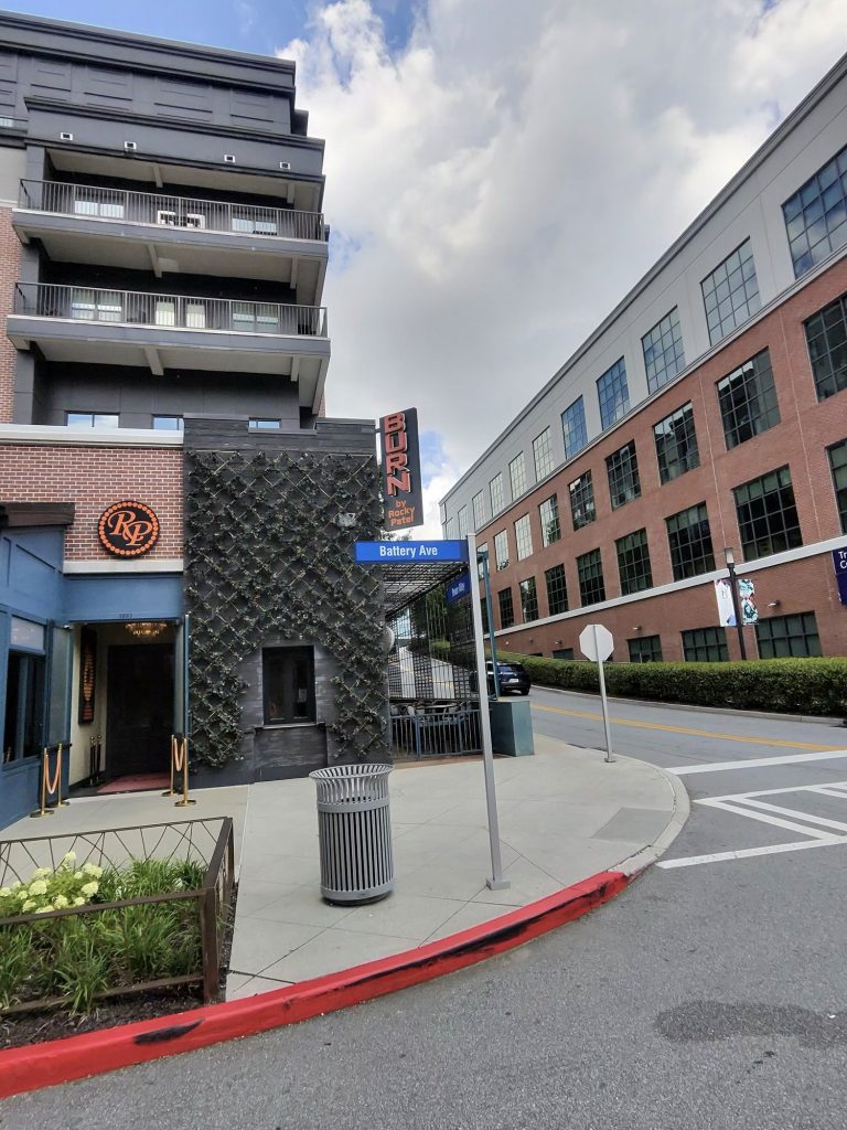 Street view of Burn by Rocky Patel at Battery Ave, showing the RP logo, vertical BURN sign, and surrounding brick and glass buildings.