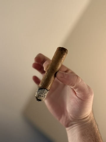 Hand holding the AJ Fernandez Amar Toro during the smoking session with a firm ash and visible wrapper damage beginning to develop.