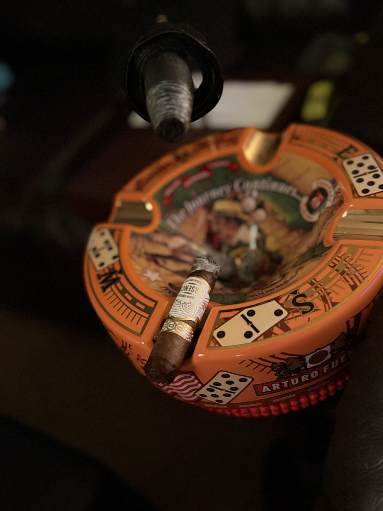 Plasencia Reserva Original Toro balanced across an Arturo Fuente ceramic ashtray beneath the cigar stand handle resting in the foreground inside The Evening Draw Lounge.