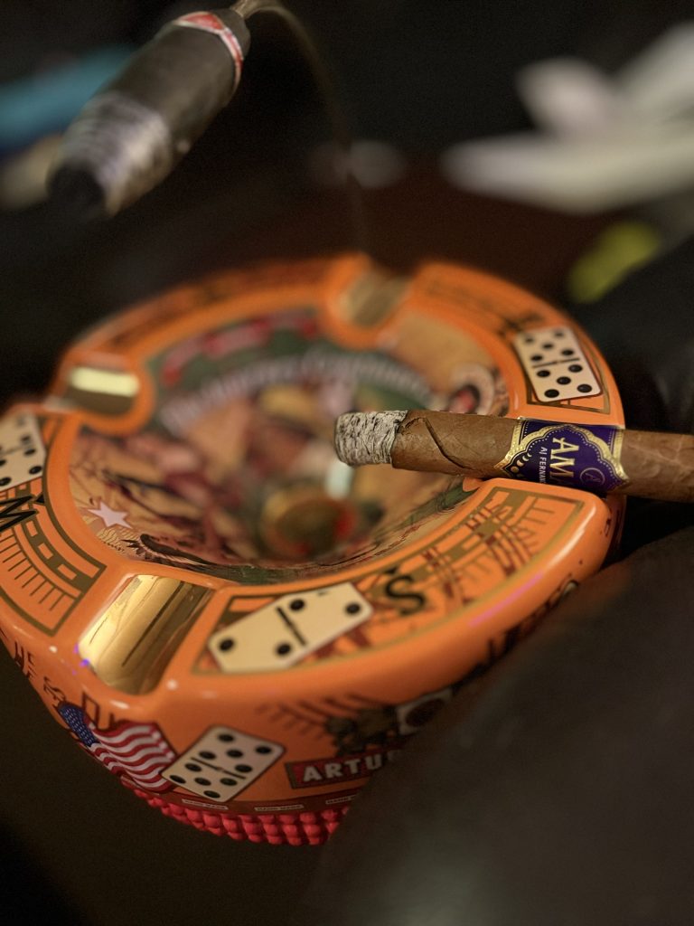 Hand holding the AJ Fernandez Amar Toro during the smoking session with a firm ash and visible wrapper damage beginning to develop.