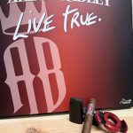 Alec Bradley Thirty Year Toro displayed with a black torch lighter and red Xikar cutter in front of an Alec Bradley “Live True” backdrop before being lit.