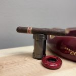 Dunbarton Mi Querida Triqui Traca Toro resting on a Hammersmith lighter beside a red cigar cutter and ashtray.