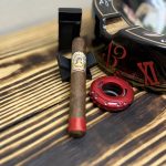 Unlit La Aroma de Cuba Original Robusto on a black cigar rest beside a red cutter, black lighter, and Arturo Fuente ashtray.