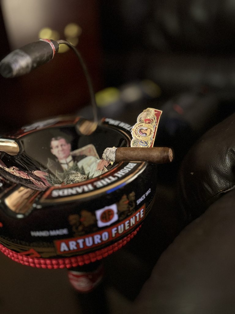 Smoking La Aroma de Cuba Original Robusto over an Arturo Fuente ashtray with its removed band standing behind the cigar.