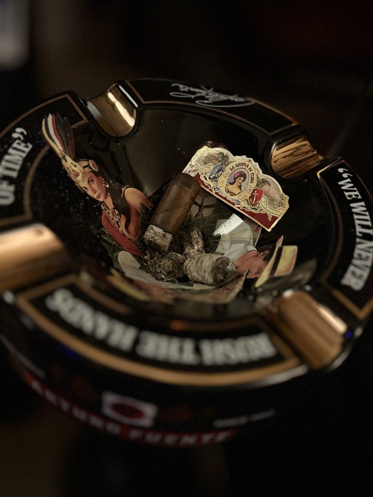 La Aroma de Cuba Original cigar nub and loose band among ashes in a black Arturo Fuente ashtray.