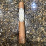West Tampa Tobacco Company White Toro before lighting with white, gray and gold bands visible.