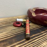 Unlit Rocky Patel 2025 Year of the Snake Toro with red and gold bands beside a red cigar cutter, lighter and ashtray.