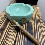 Macanudo Café Prince Philip Churchill resting on a black cigar stand beside a green Macanudo ashtray.
