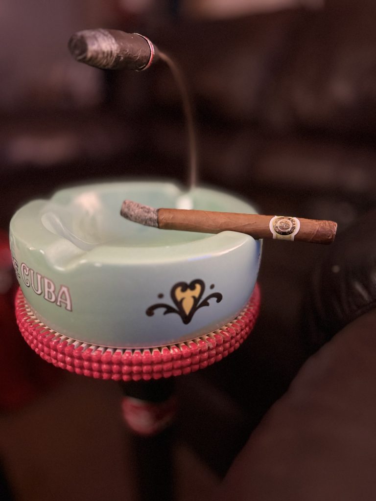 Lit Macanudo Café Prince Philip Churchill resting across a green Macanudo ashtray with smoke rising above it.