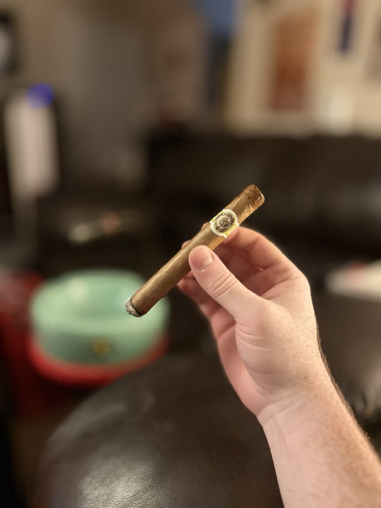 Partially smoked Macanudo Café Prince Philip Churchill held by hand inside The Evening Draw lounge.