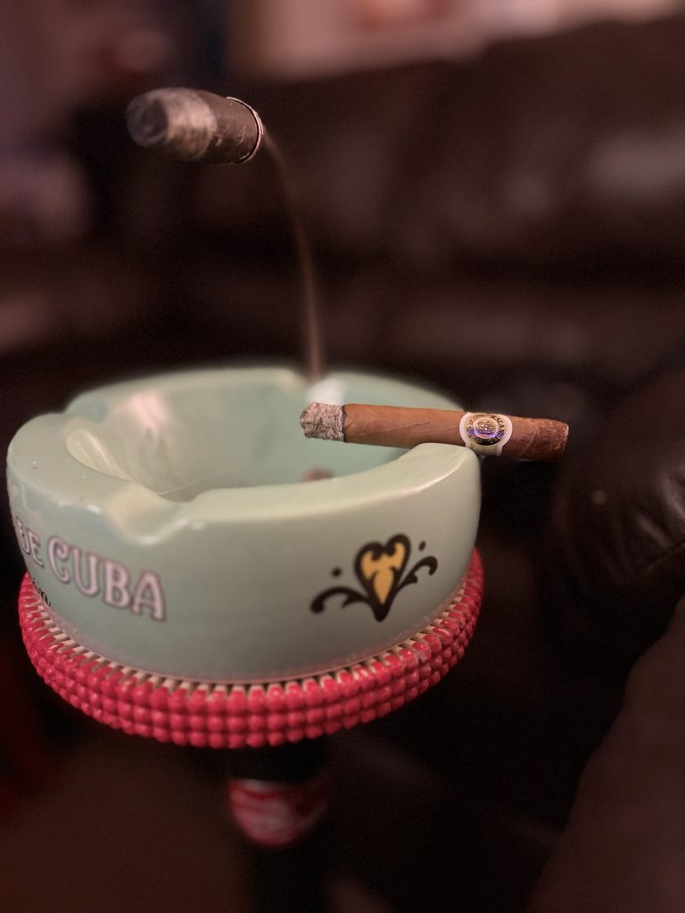 Macanudo Café Prince Philip Churchill with a firm gray ash resting across a green ashtray.