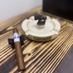 Unlit J.C. Newman Diamond Crown Julius Caeser Toro resting on a black cigar stand beside a Buffalo Trace ashtray.