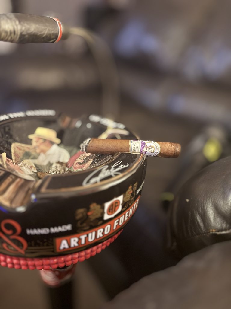 Lit Diamond Crown Julius Caeser Toro resting across a black Arturo Fuente ashtray with smoke rising from the foot.