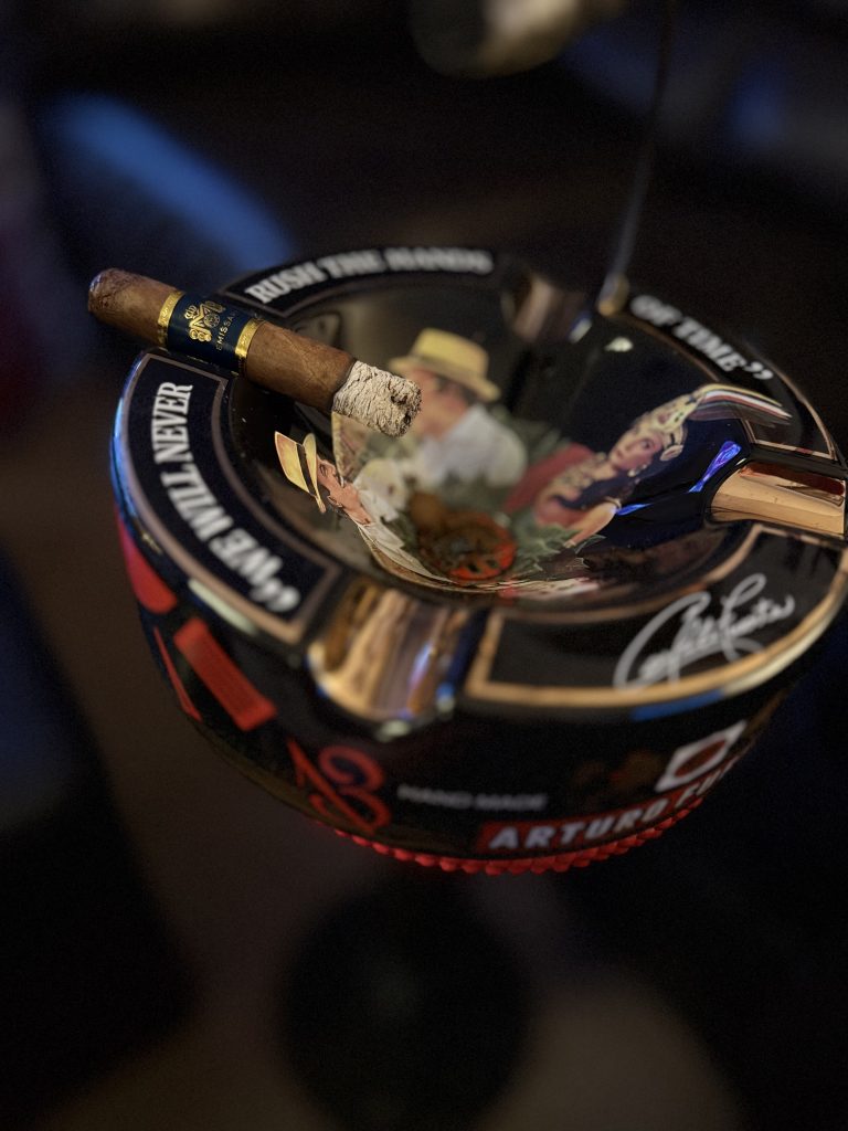 Macanudo Emissary España Robusto resting across a black Arturo Fuente ashtray with a solid white ash.