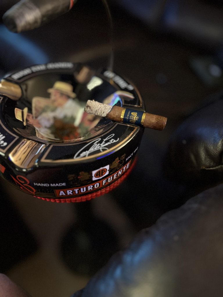 Macanudo Emissary España Robusto resting on an Arturo Fuente ashtray later in the smoke with a long textured ash.