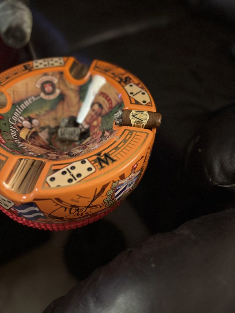 AVO Classic Natural Robusto late in the smoke resting on an orange Cuban-themed ashtray beside accumulated cigar ash.