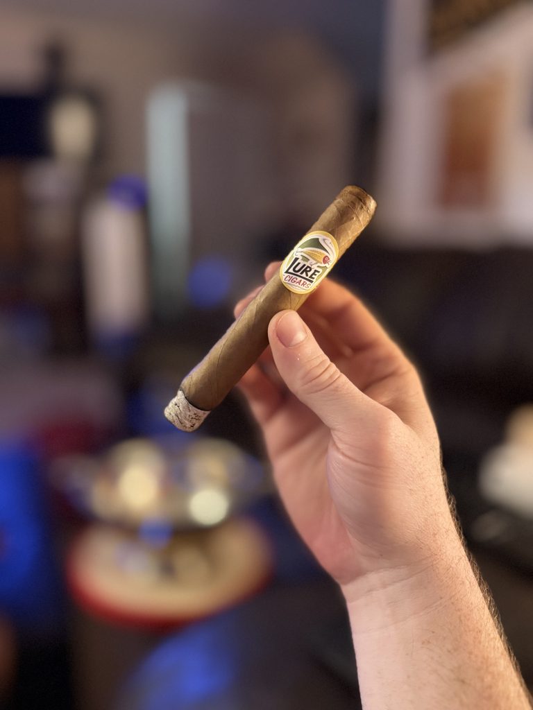 Lit Lure Cigars Tally Allie Habano Toro held by hand with a long white ash during the smoking session.
