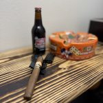 Foundation Olmec Claro Toro resting on a black cigar stand with an IBC Root Beer bottle and orange cigar ashtray in the background.