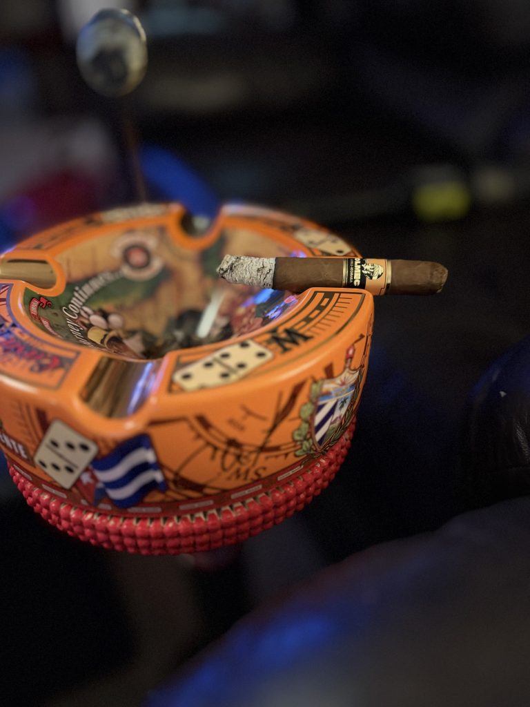 Lit Foundation Olmec Claro Toro with a developed gray ash resting across an orange cigar ashtray.