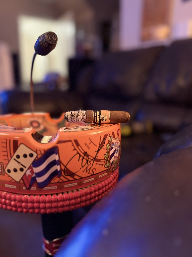 Foundation Olmec Claro Toro burning in an orange cigar ashtray with lounge lighting in the background.