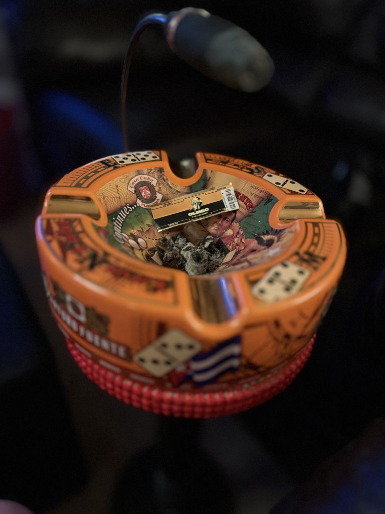 Foundation Olmec Claro cigar band lying among ashes inside a bright orange cigar ashtray.
