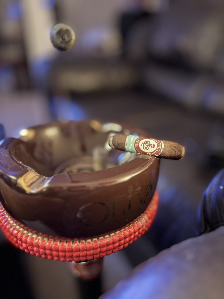 League of Fat Bastards Serie O Toro resting across an Oliva ashtray as a section of cigar ash falls above it.