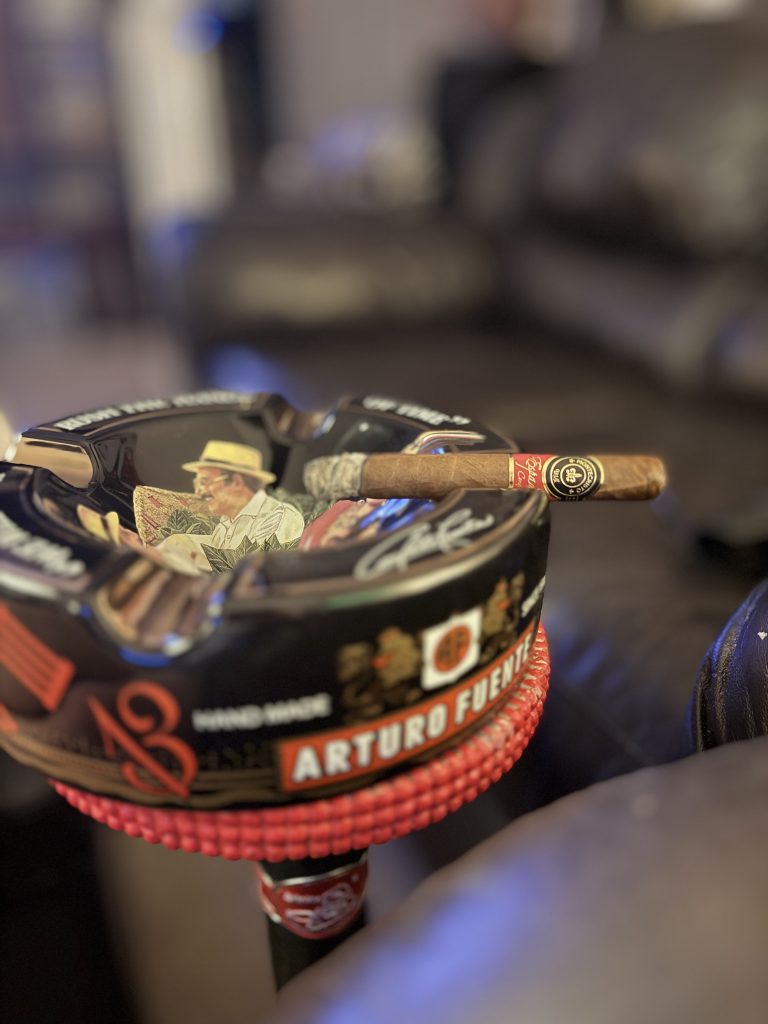 Lit Montecristo Espada Conquistador Toro resting across a black Arturo Fuente ashtray with a compact gray ash.