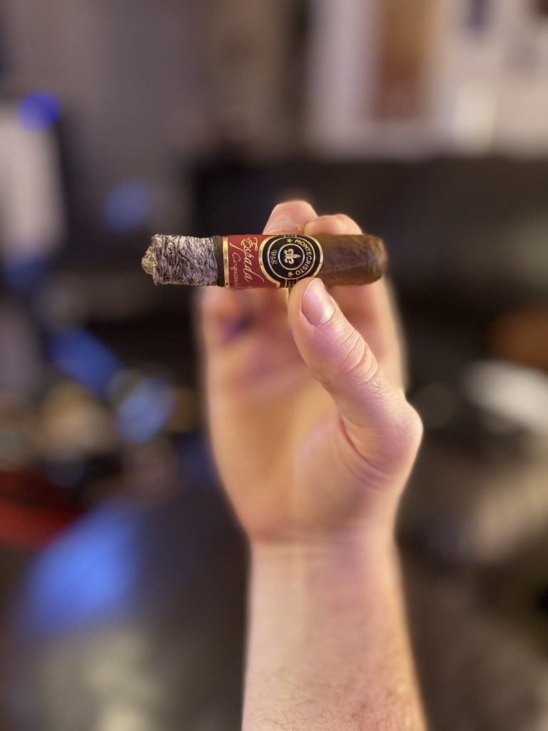 Hand holding the shortened Montecristo Espada Conquistador Toro with a long, layered ash near the final third.