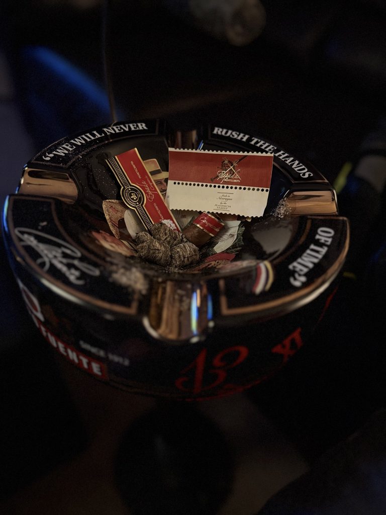 Montecristo Espada Conquistador paper sleeve, cigar bands, ashes, and smoked remnants collected inside a black Arturo Fuente ashtray.
