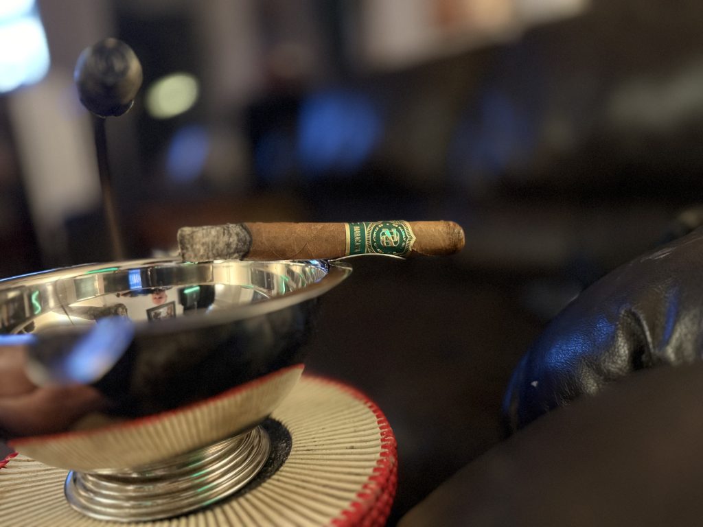 OZ Family Maracana Toro resting across a polished silver ashtray with long dark ash