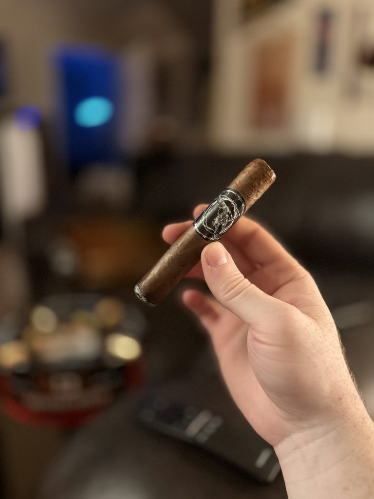 Black Label Trading Co Lawless Robusto held in hand shortly after lighting with its black skull band visible.