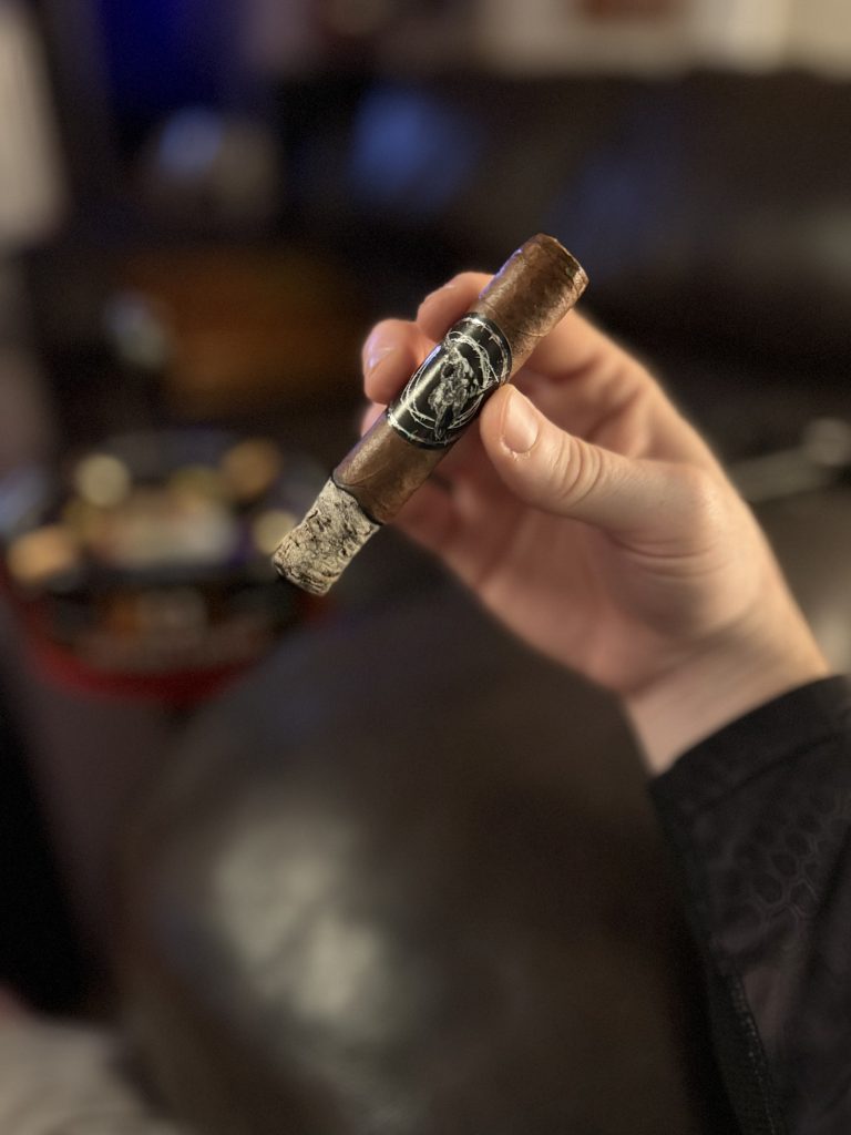 Lit Black Label Trading Co Lawless Robusto held in hand with a long gray ash during the first portion of the smoke