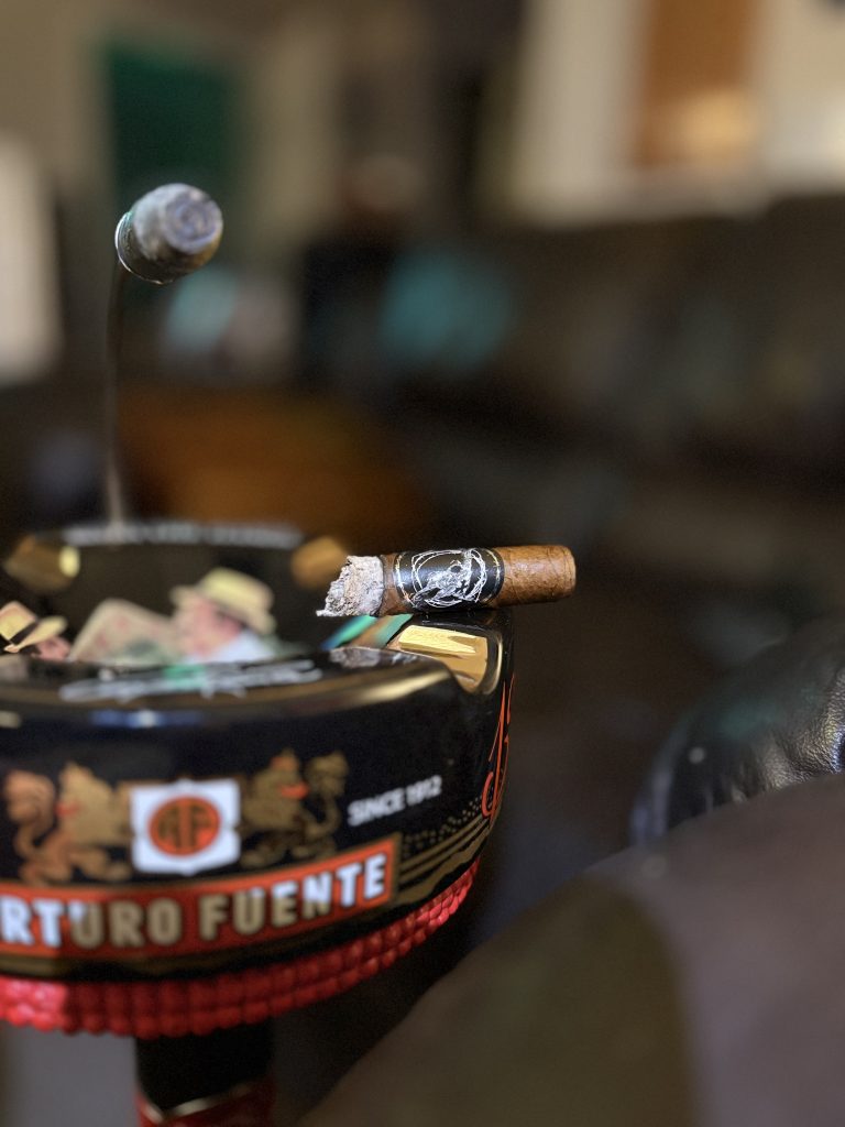 Black Label Trading Co Lawless Robusto burning on the edge of an Arturo Fuente ashtray with smoke rising above it